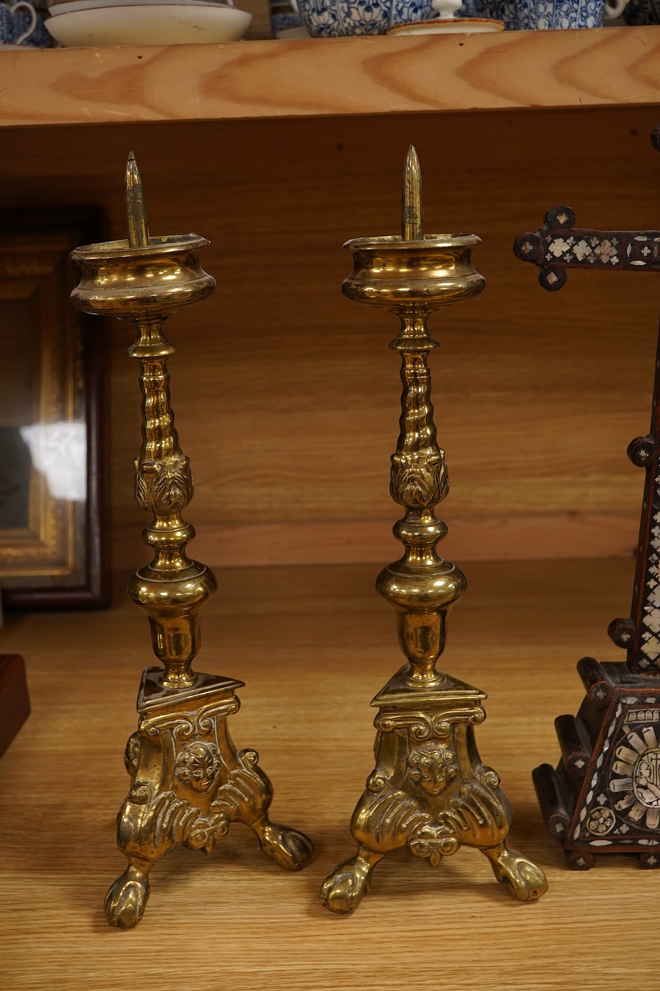Two 19th century walnut and mother-of-pearl inlaid crucifixes and a German ebonised and white and metal mounted crucifix and a pair of Dutch or German brass tripod base cricket candlesticks, largest 56cm high (5)